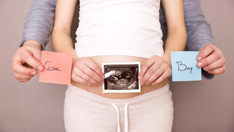 Pregnant woman with her husband holding ultrasound scan and blue and red post its with words boy or girl