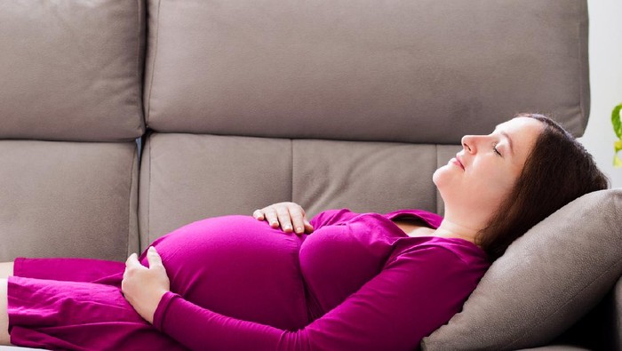 Portrait of a tired pregnant woman sleeping on a couch in the living room at home