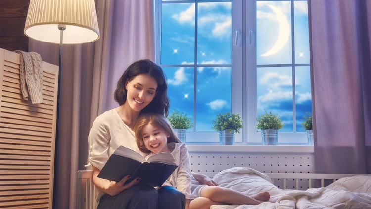 Father reading a book to his daughter while lying on the floor in bedroom