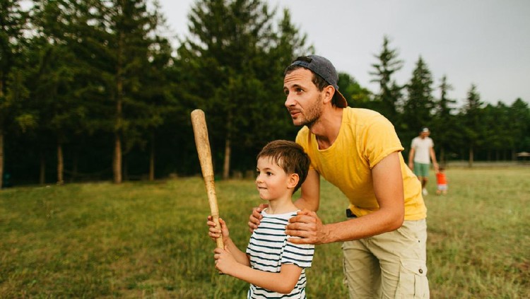 Young father sharing basics of baseball with his little boy, outdoors in the park