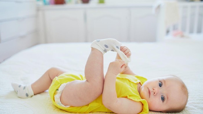 Adorable two months baby girl relaxing in bedroom on knitted blanket on a sunny morning