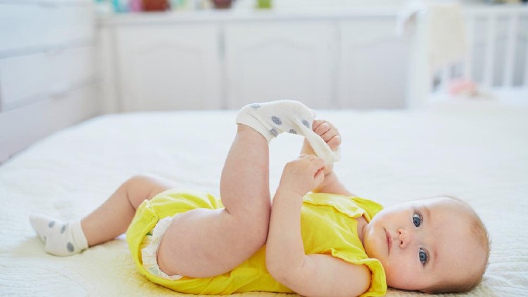 Adorable two months baby girl relaxing in bedroom on knitted blanket on a sunny morning
