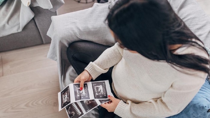 One woman, beautiful pregnant woman sitting at home, holding ultrasound pictures.