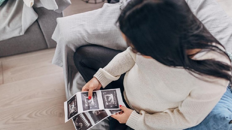 usg One woman, beautiful pregnant woman sitting at home, holding ultrasound pictures.