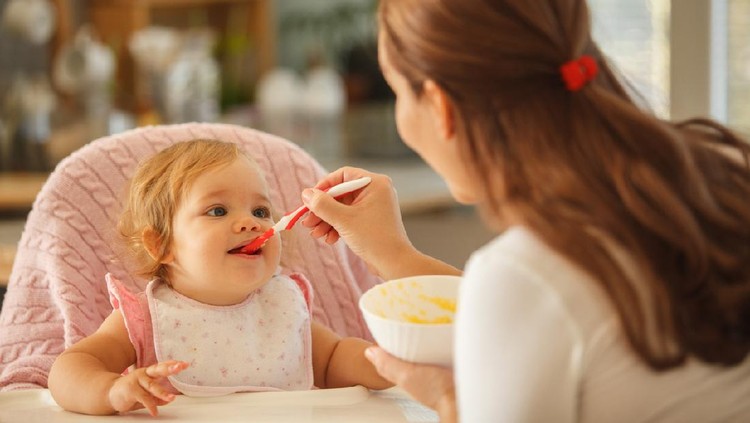 Close-up shot of mother spoon feeding her baby girl.