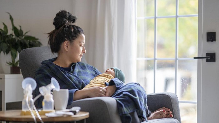 Tired mother holding her newborn child at home after tying to pump.