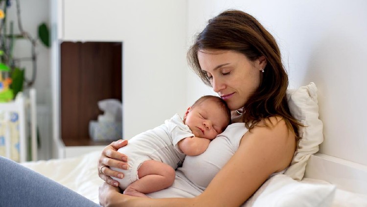 Tired mother holding her newborn child at home after tying to pump.