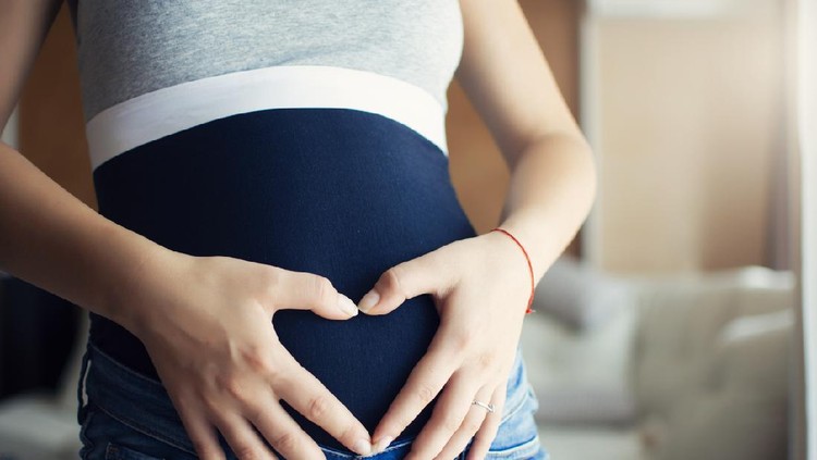 Picture of young pregnant woman in her home holding hands on belly