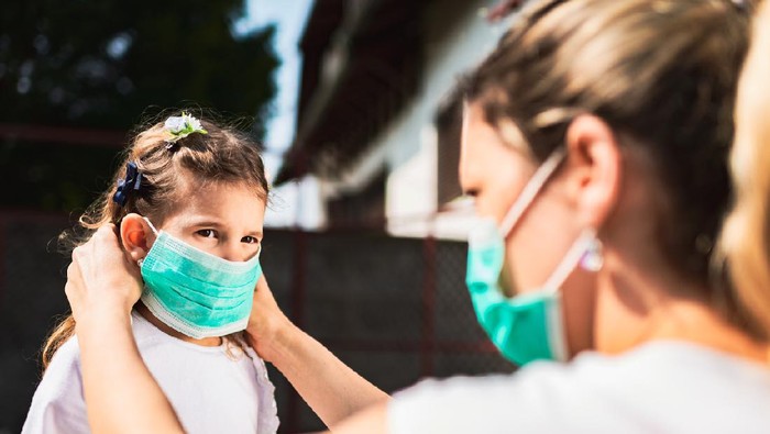 Single mother applying pollution mask to her daughter. They are outside.