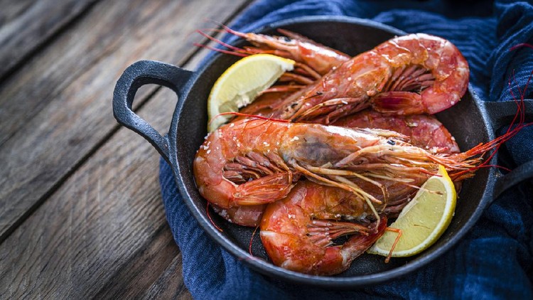 Udang Seafood: high angle view of fresh shrimps in a cast iron cooking pan shot on rustic wooden table. Predominant colors are red, blue and brown. High resolution 42Mp studio digital capture taken with Sony A7rii and Sony FE 90mm f2.8 macro G OSS lens