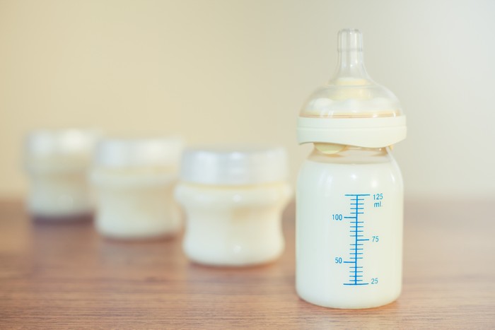 Baby bottle with milk and a measuring scale on the background of a lot of full bottles of breast milk. Mother's milk - the most healthy food for newborn