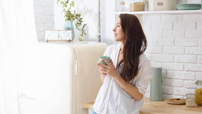 Young happy woman drinking coffee on the kitchen in the morning.