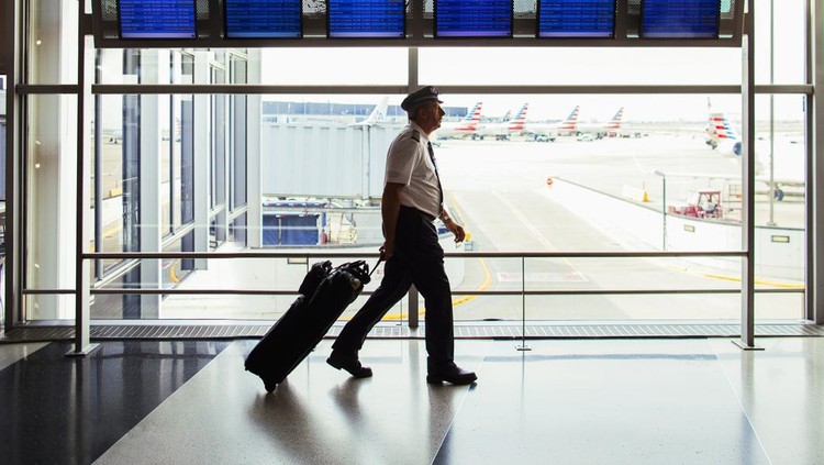 Chicago, IL, USA - July 17, 2017: Pilot walking through O'Hare Airport terminal with the arrivals and departures board in background.