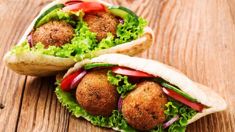 Falafel and fresh vegetables in pita bread on wooden table