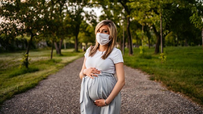 Portrait of young pregnant woman in public park with protective face mask.