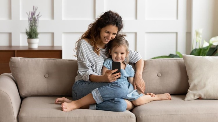 1207723205 Front view happy pretty mommy cuddling small kid daughter, taking selfie shot on smartphone or playing online game at home. Loving young mother embracing little child, using mobile apps together.