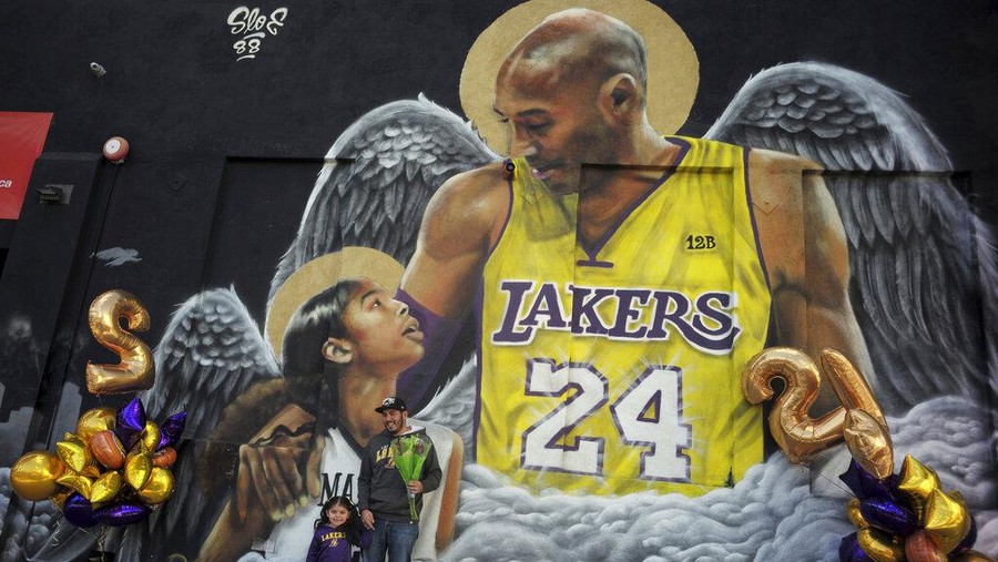 Kobe Bryant Jose Jara with his three-year-old daughter Giana poses for a picture in front of a mural on the side of Hardcore Fitness along Pico Blvd as fans of Kobe Bryant celebrate the life and legacy around murals and makeshift memorials in Los Angeles on Tuesday, Jan. 26, 2021. (Keith Birmingham/The Orange County Register via AP)
