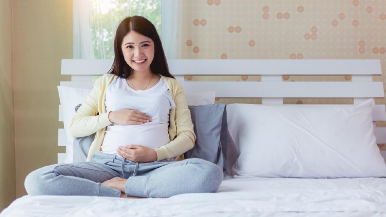 Happy pregnant mother touching beautiful belly with love, smile face on bed at home. prenatal, pregnancy, motherhood, expect concept. Young pregnancy girl and baby or fetus has good health, copy space