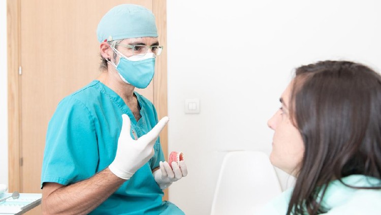 Male dentist explaining the situation to a patient with double mask during coronavirus pandemic.