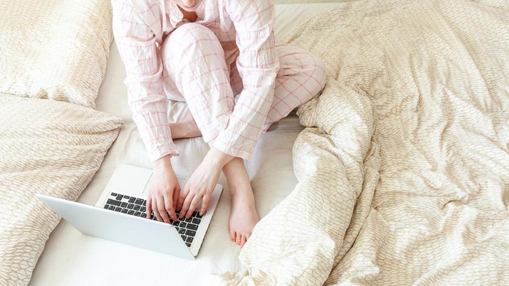Mobile Office at home. Young woman in pajamas sitting on bed at home working using on laptop pc computer. Lifestyle girl studying indoors. Freelance business quarantine concept