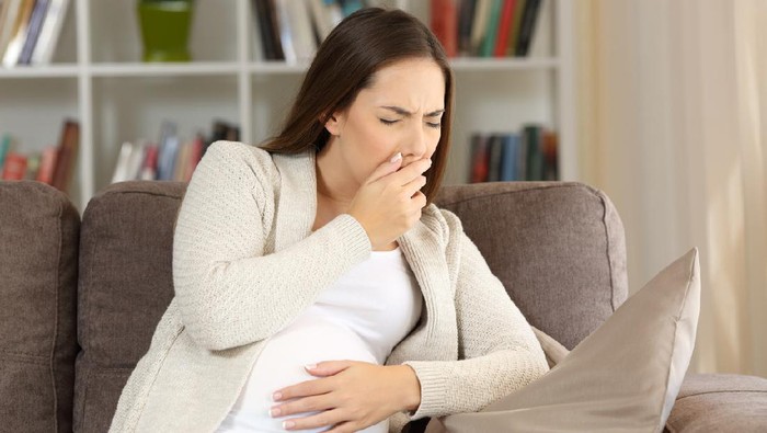 Pregnant woman suffering nausea sitting on a sofa at home