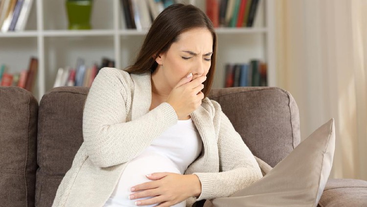 Pregnant woman suffering nausea sitting on a sofa at home