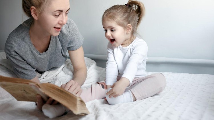 Pretty Young Happy mom shows illustration in book to her little surprised daughter. Loving family concept
