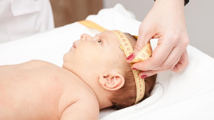 Close-up shot of pediatrician examines two months baby boy. Doctor using measurement tape checking baby head size