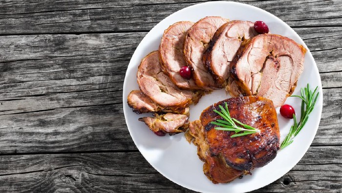slices of delicious barbecue turkey roulade with cranberry and rosemary on white dish on old dark wooden table, view from above, close-up