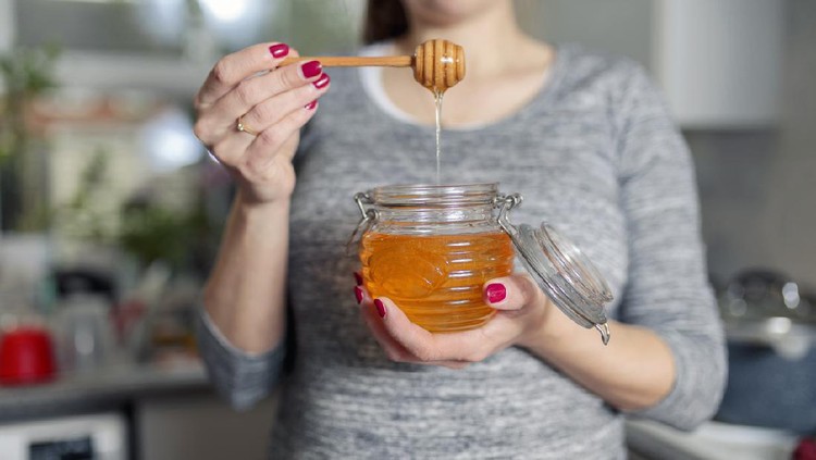 Woman holding jar of honey in kitchen