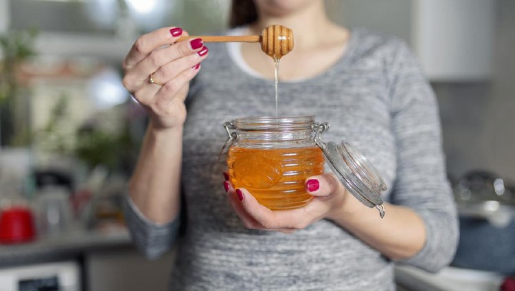 Ilustrasi makan madu Woman holding jar of honey in kitchen