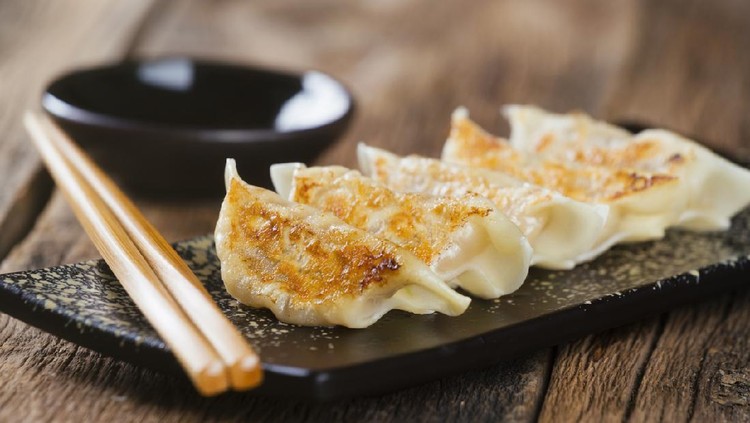 A plate of authentic Japanese gyoza potsticker appetizers with dipping sauce and chopsticks, against a wooden background.