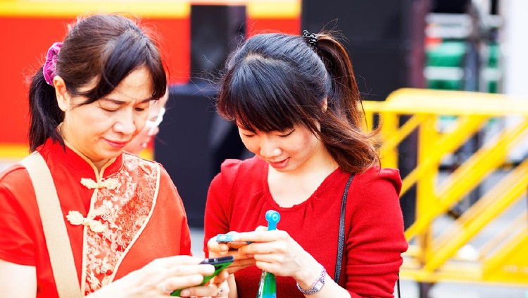 Bangkok, Thailand - February 19, 2015: Red dresses Thai women in Yaowarat Road at chines enew year. Mature and young women both are using mobiles. Mature woman is wearing traditional chinese styled shirt.