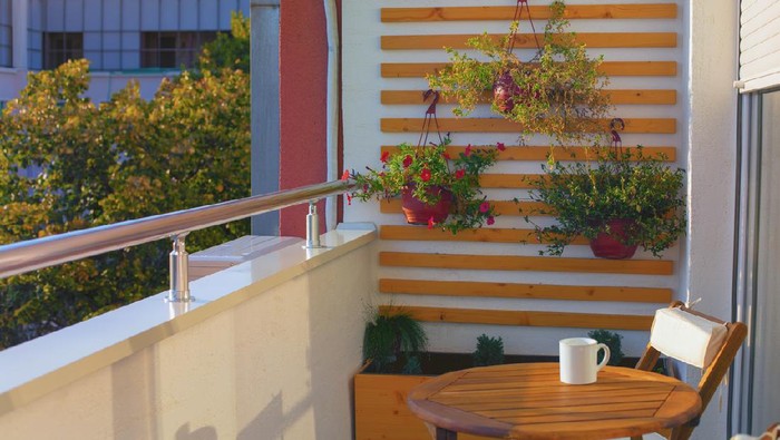 Beautiful sunny afternoon on a modern balcony with wooden coffe table, chairs, coffee cup and vertical garden.