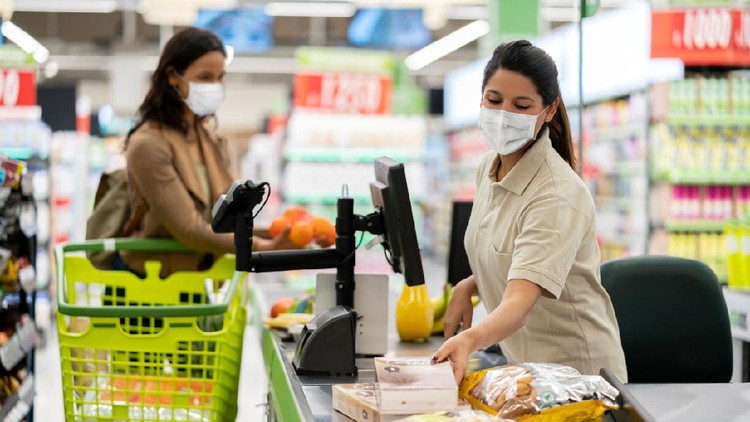 Latin American cashier scanning products at a grocery store wearing a facemask - quarantine lifestyle concepts