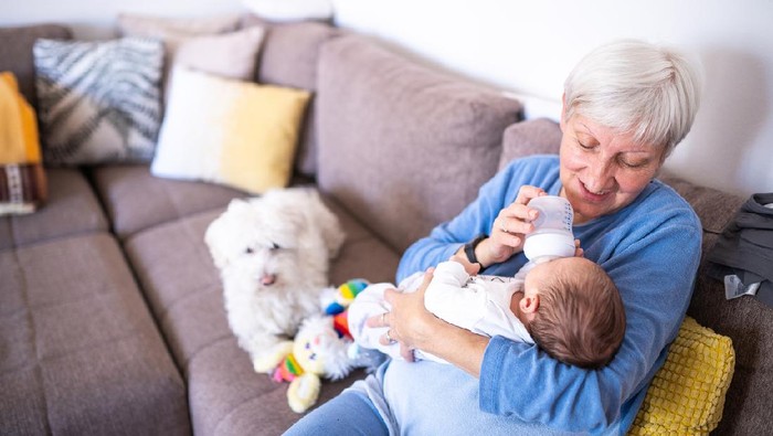 Grandmother holding little grandson in the room at home. Senior woman hold little baby cute smiling. Happy grandmother with her grandchild in home.
