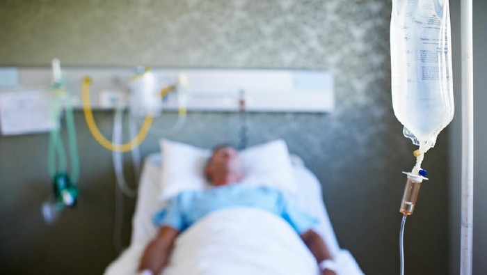 Closeup shot of an IV drip with an unconscious patient in the background