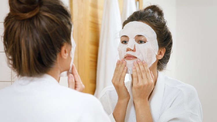 Woman is applying sheet mask on her face in the bathroom