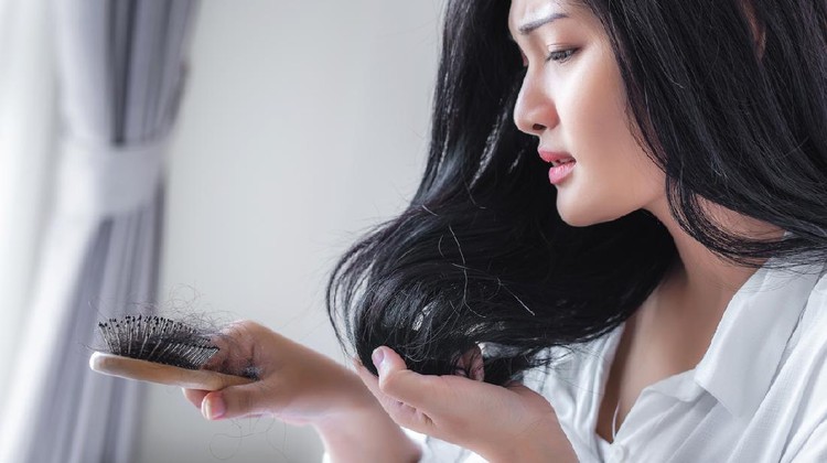 Attractive Asian woman serious about her brush for presentation hair loss problem and looking at comb