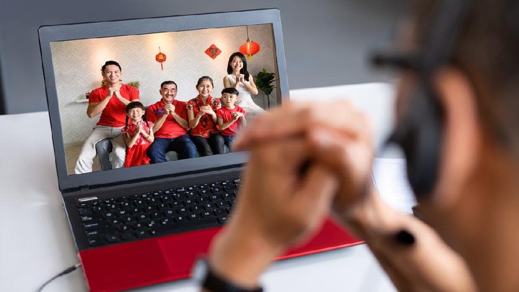 Multi-generation Asian Chinese family greeting family member working abroad with video call on laptop computer in Chinese New Year during lockdown quarantine and MCO (Movement Control Order) on global pandemic. Covid-19 and Coronavirus, 5G & Wireless Technology, Chinese New Year Celebration and Chinese Traditional Festival, Family Bonding and Togetherness Concepts.