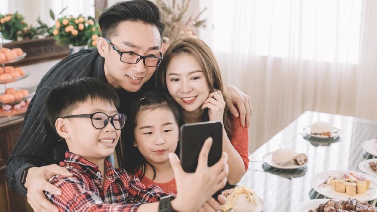 an asian chinese boy taking selfie photography using his mobile with his family during chinese new year's eve family reunion dinner