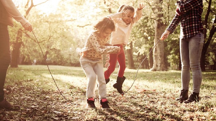 Cheerful family playing with jump rope together in park.