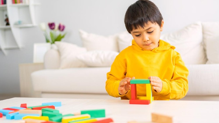 Little cute kid is playing colorful wooden blocks game home in the living room.  Having fun and learning creativity.