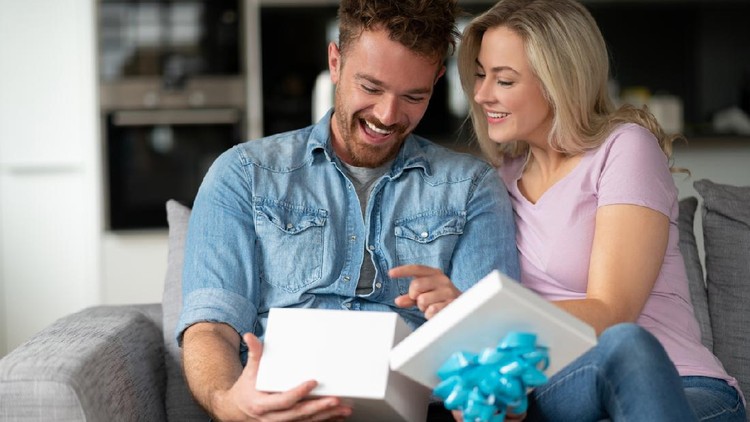 Portrait of a very happy man opening a gift from his girlfriend at home and smiling - anniversary concepts