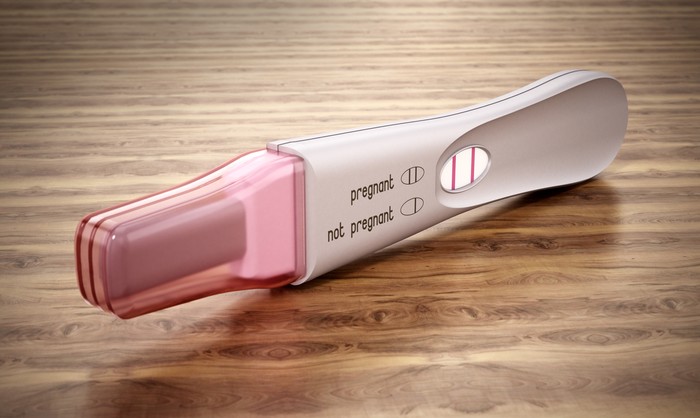 Pregnancy test stick with two stripes standing on wooden table.