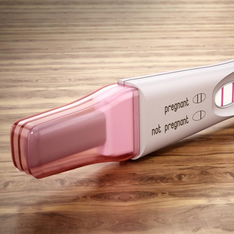 Pregnancy test stick with two stripes standing on wooden table.