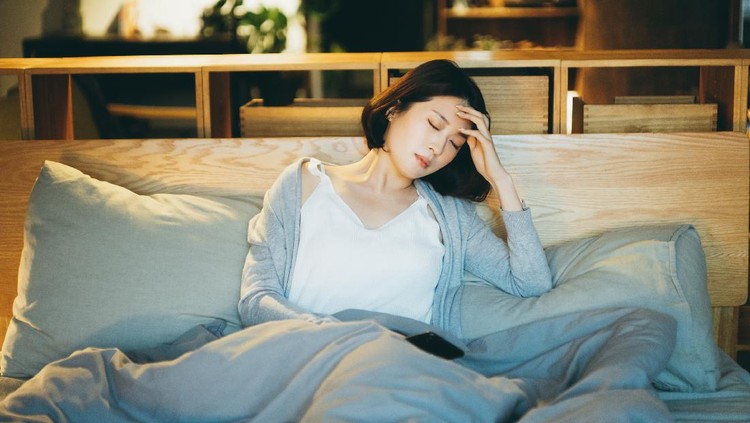 Young Asian woman feeling sick and suffering from a headache, lying on the bed and taking a rest at home