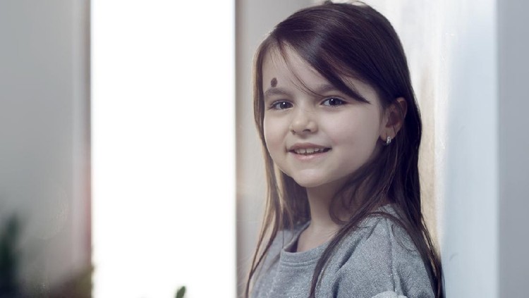 little girl with brown hair smiling indoors,looking at camera.horizontal shot, casual wear.