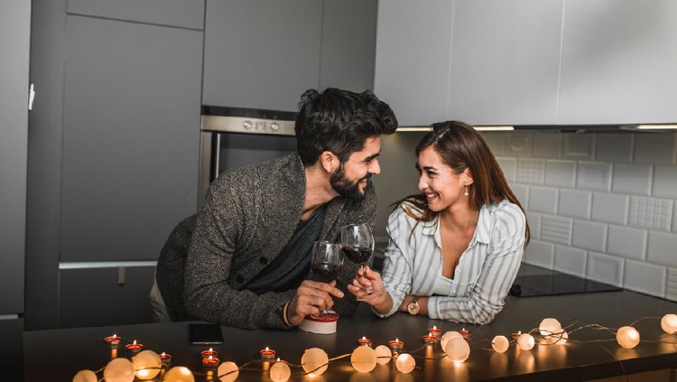 Beautiful young couple is having a romantic moment in their home and they are toasting with wine