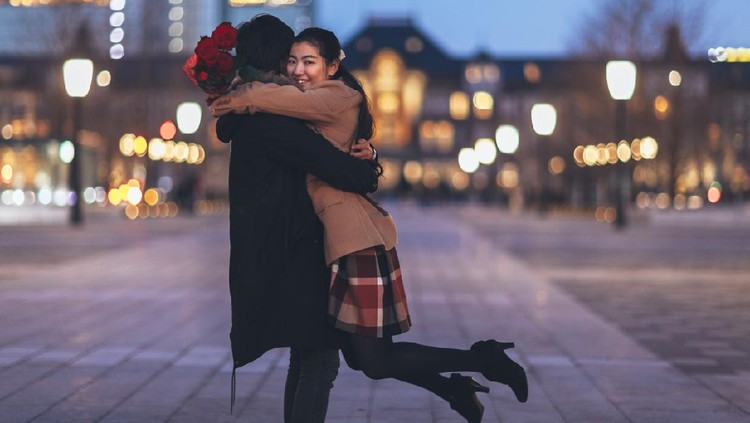 A happy Japanese couple is hugging each other in the street at night.